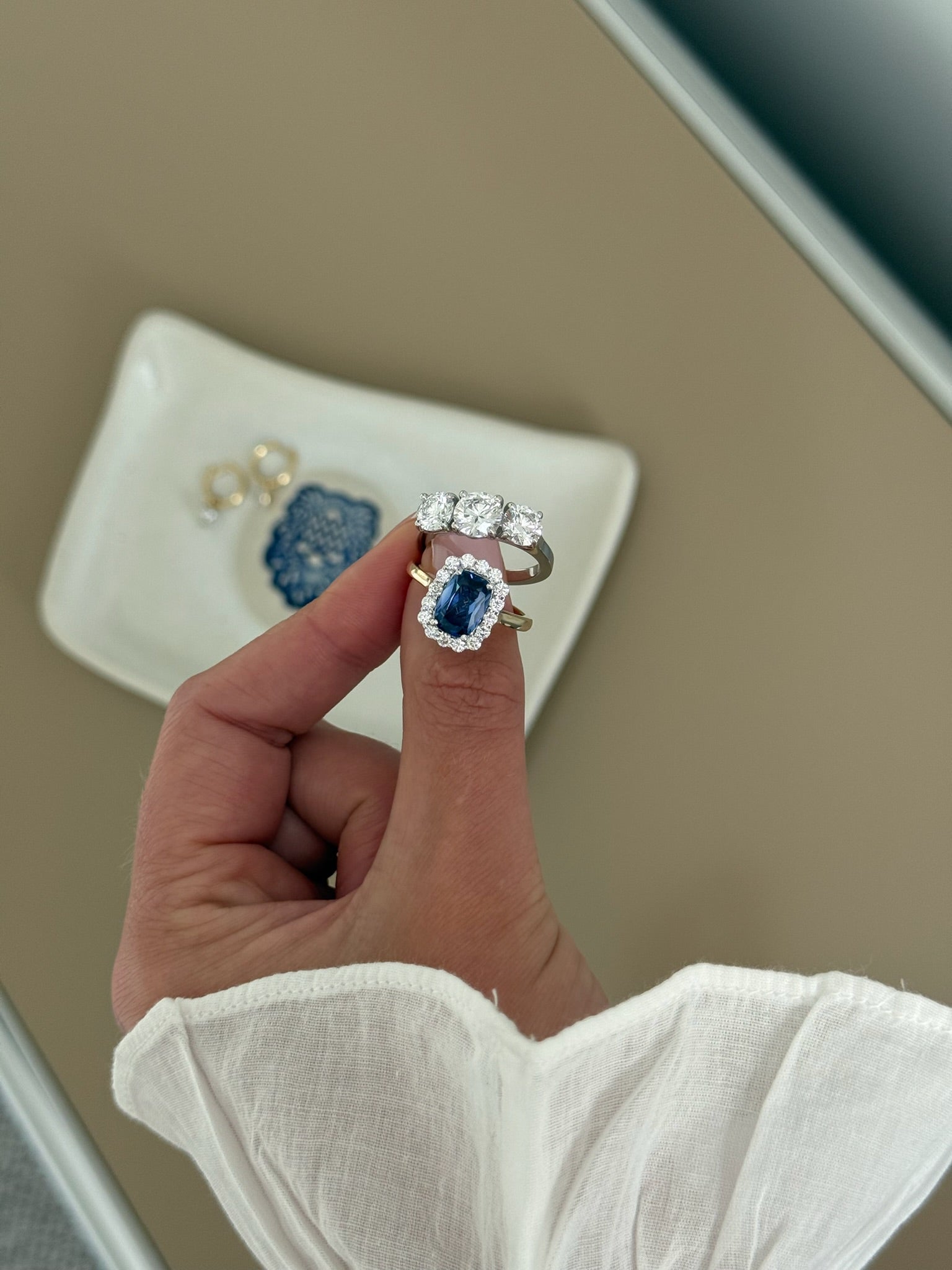 A close-up of a hand wearing a ring with a large blue sapphire surrounded by a halo of small clear stones, set on a gold band. 