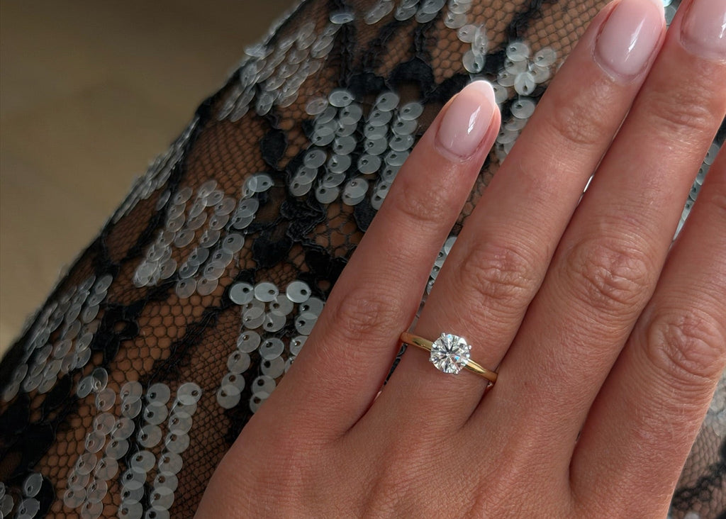 Hand wearing a gold ring with a diamond on a patterned fabric background