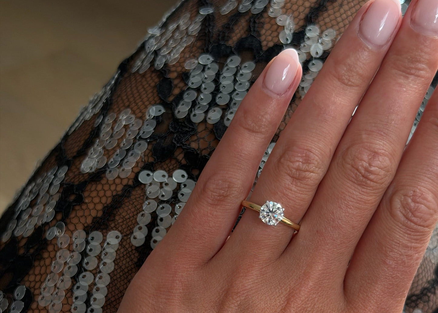 Hand wearing a gold ring with a diamond on a patterned fabric background