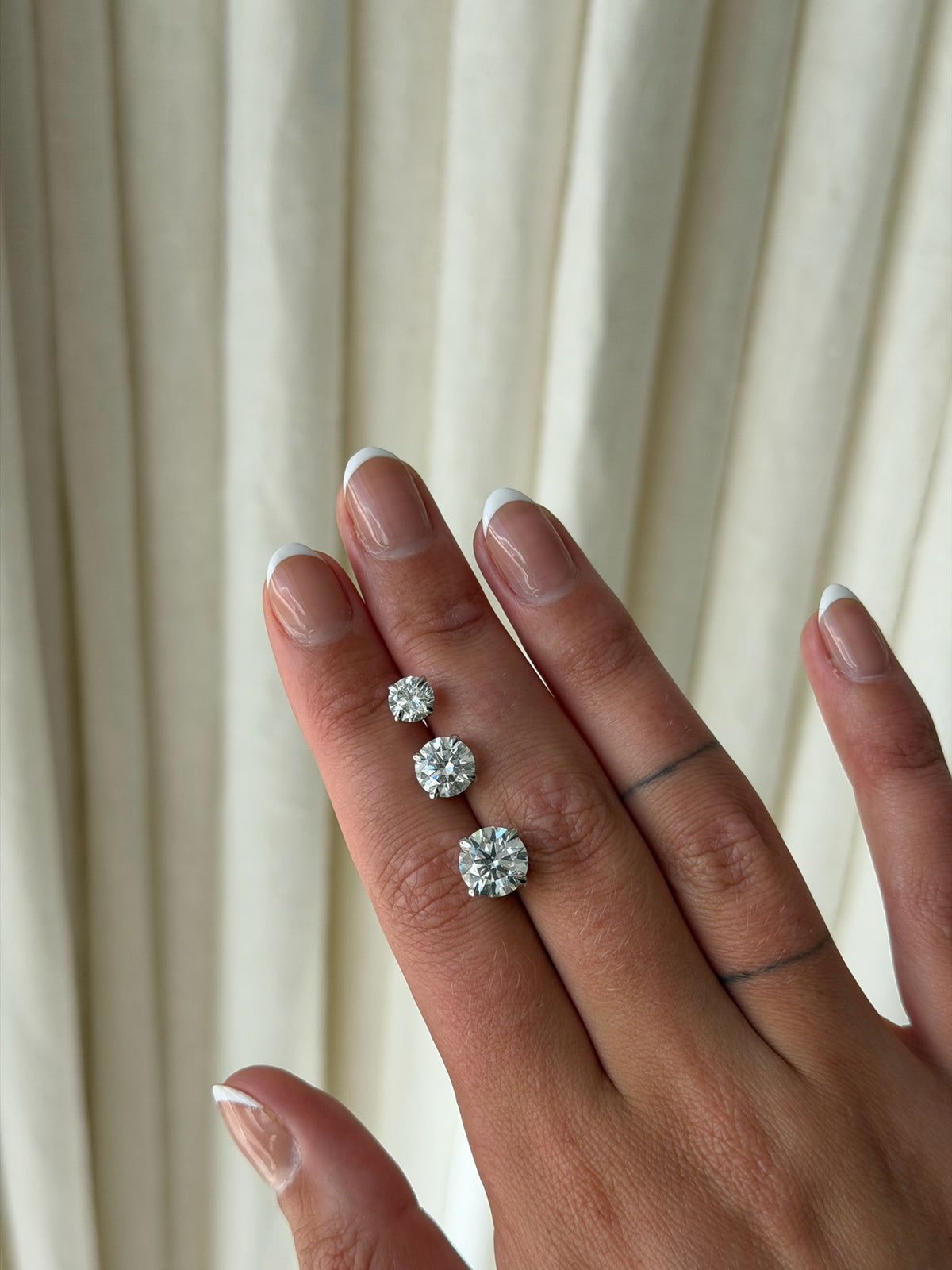 Hand holding three diamond studs to show diamond size difference