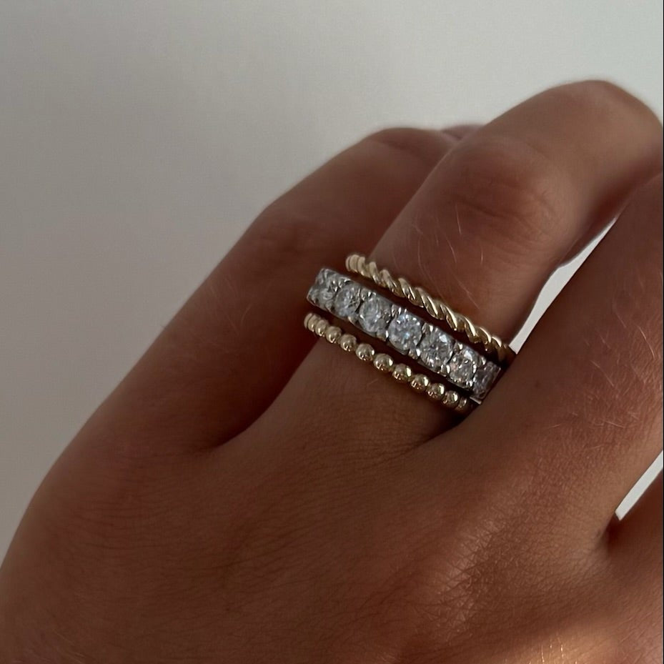 Hand wearing a bracelet and rope ring with a neutral background