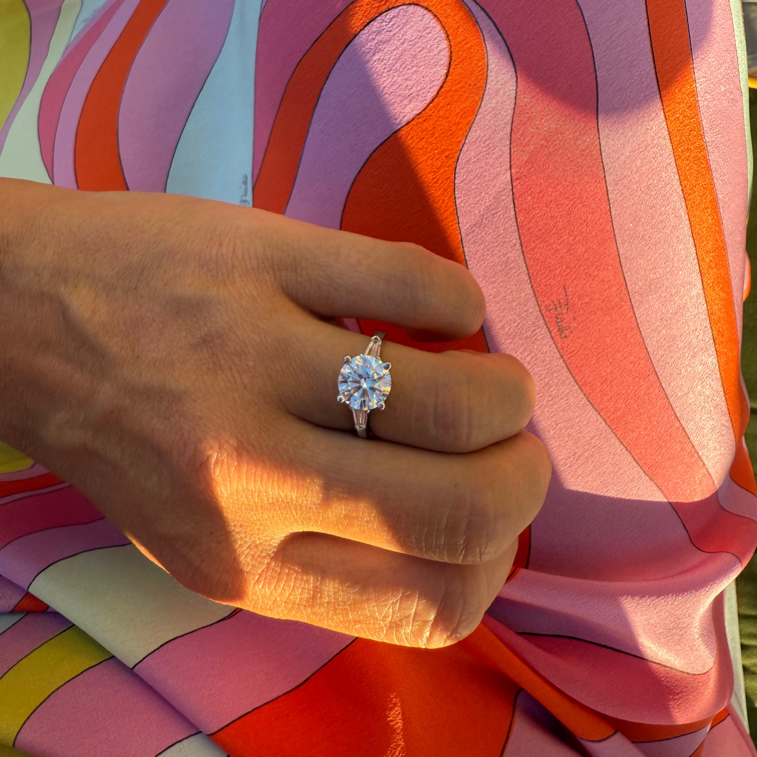 Close-up of a hand wearing a diamond ring against a Pucci dress.