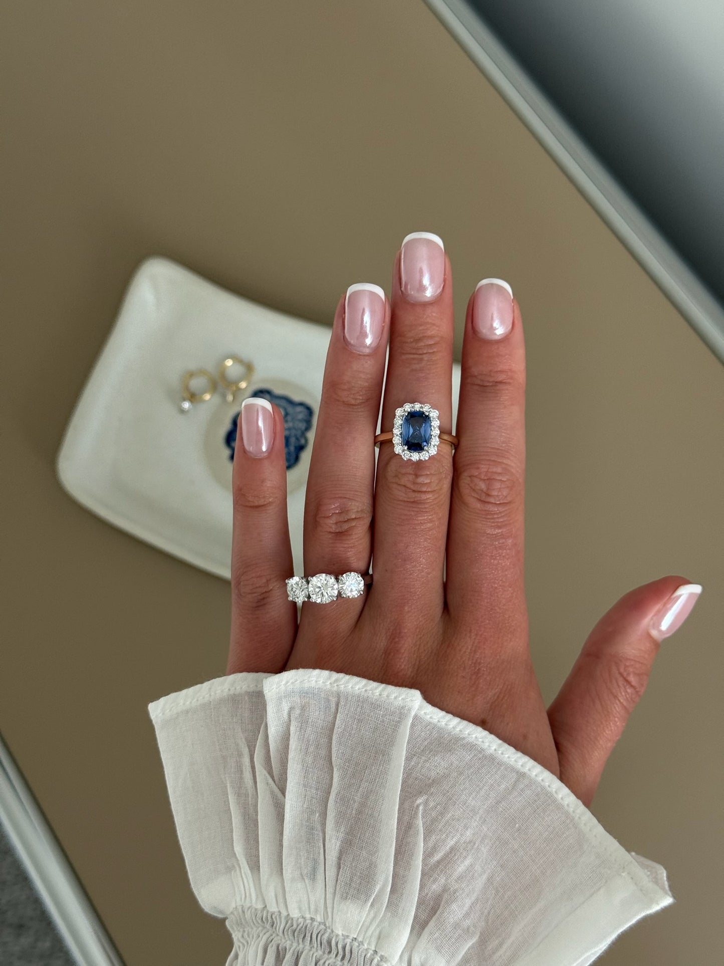 A close-up of a hand wearing a ring with a large blue sapphire surrounded by a halo of small clear stones, set on a gold band. 